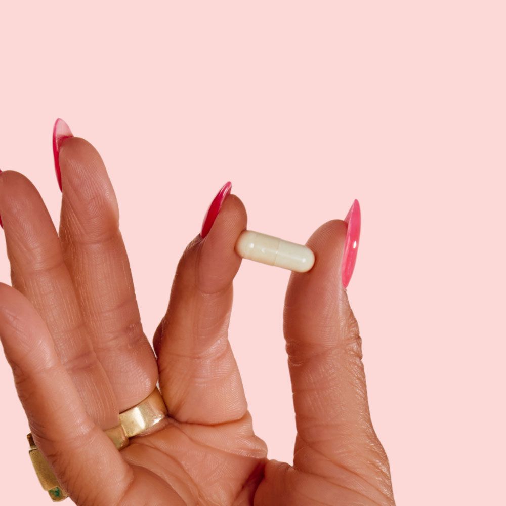 A close up of a woman's hand holding a Boric Acid Suppository in front of a pink background