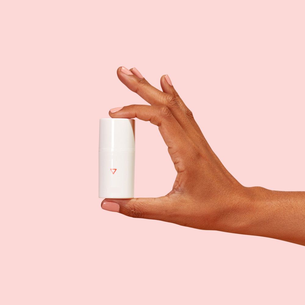 A woman's hand holding a Wisp pump bottle in front of a pink background