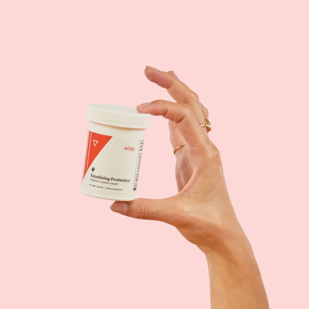 A woman's hand holding Wisp Equalizing Probiotics in front of a pink background