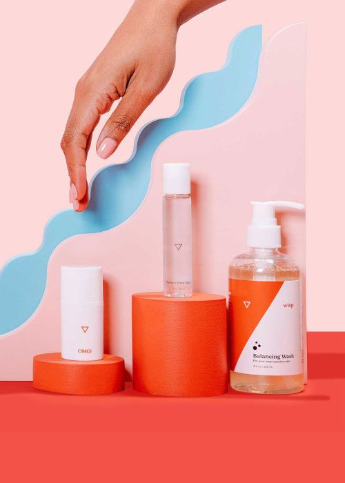 woman's hand reaches for Wisp OMG! Cream, Harmonizing Lube, and Balancing Wash sitting on colorful geometric background