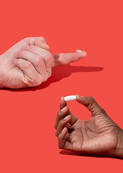Hands holding pill to and topical cream to treat genital herpes on a red background