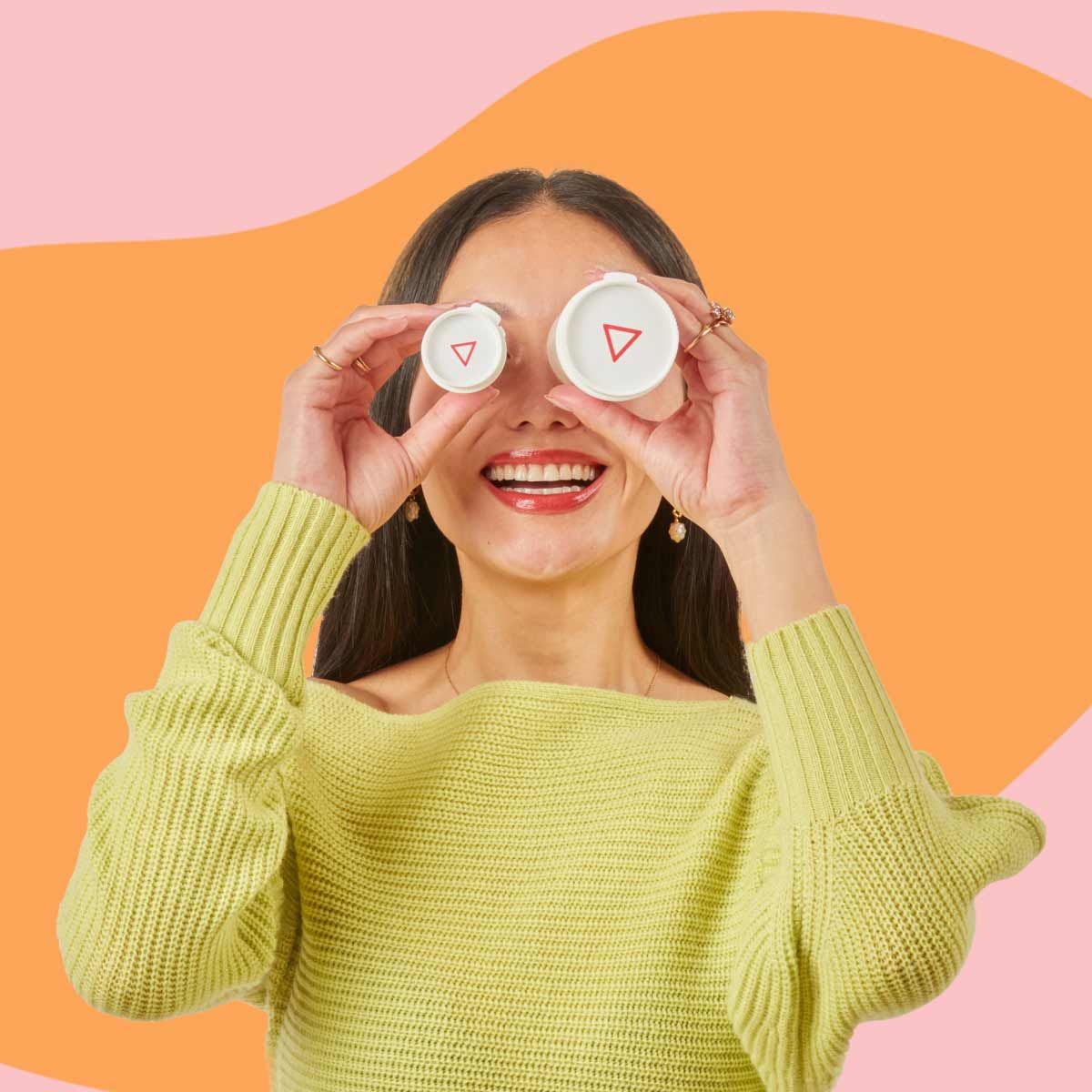 A smiling woman holds Wisp prescription vials for BV and Yeast treatment in front of her eyes