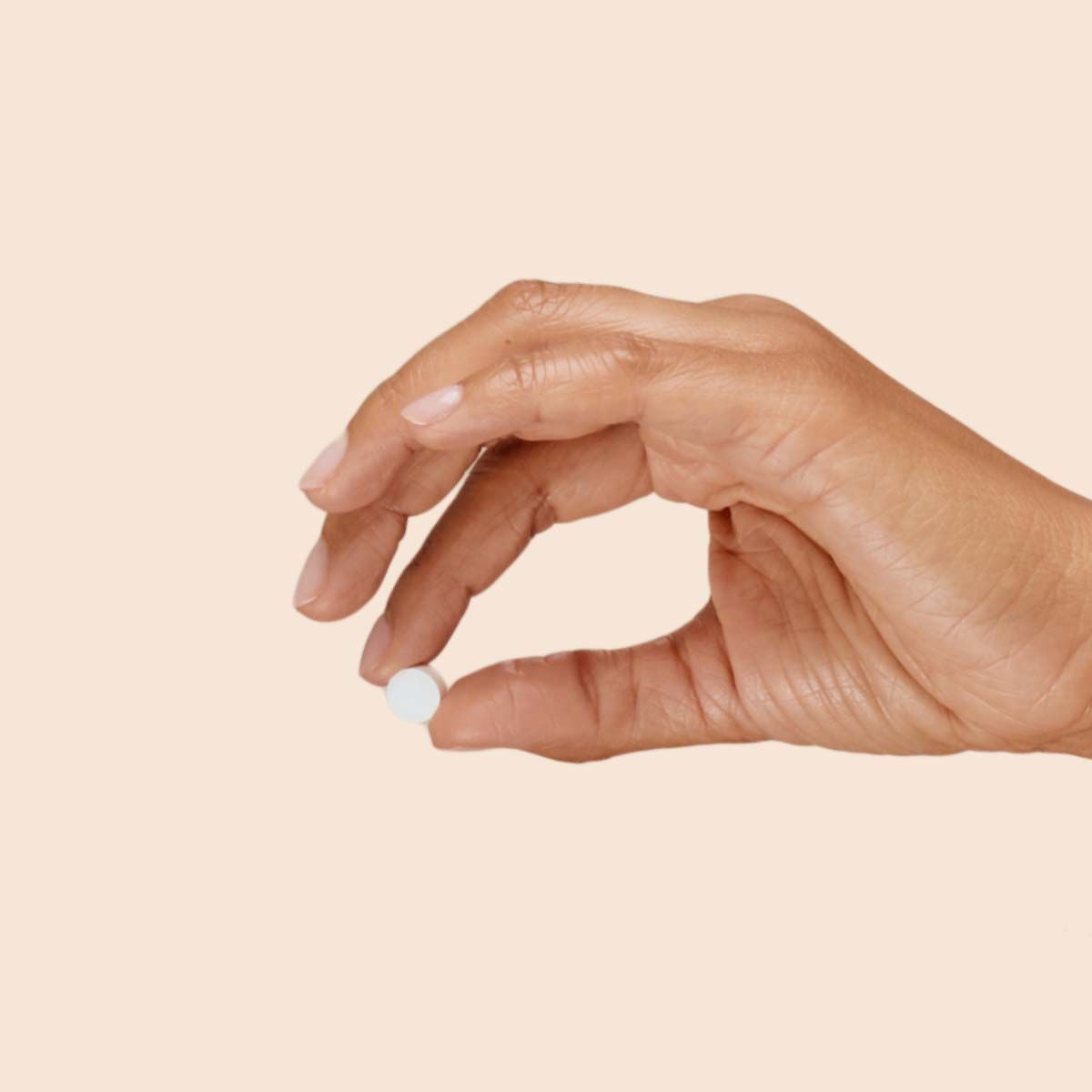 A woman's hand holding a pill with a cream background
