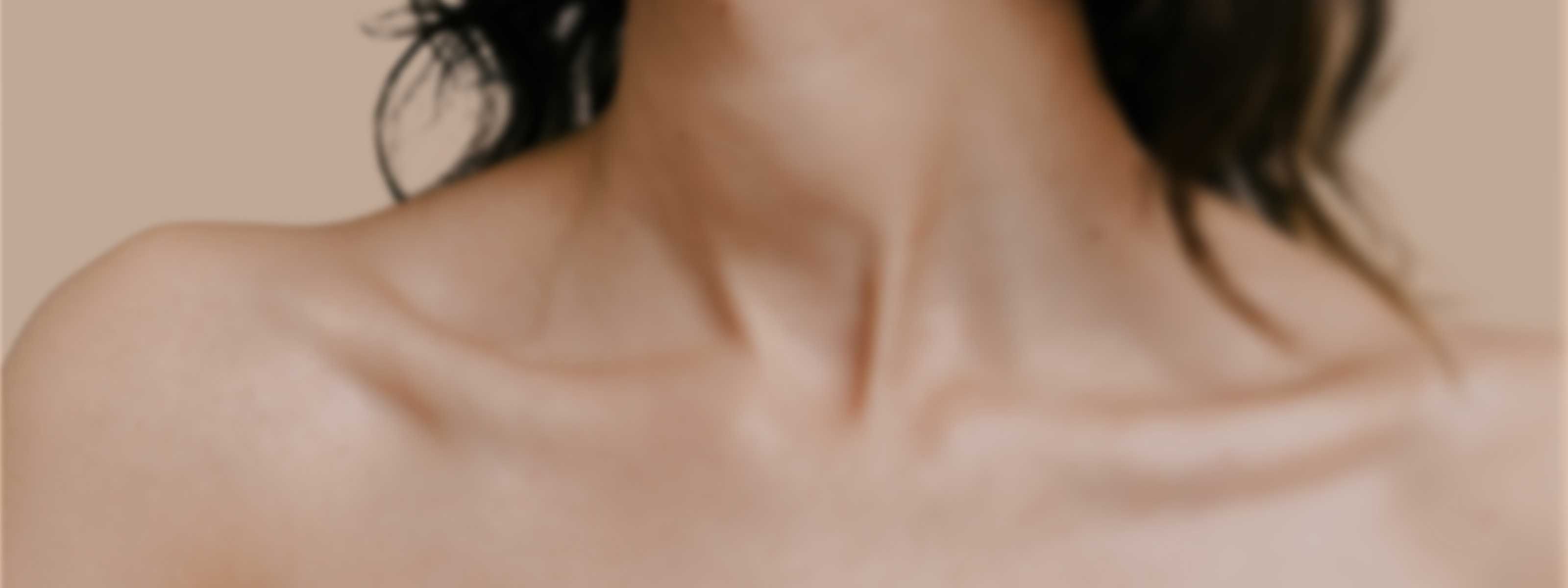 Close up of the neck and shoulders of a woman against a beige background