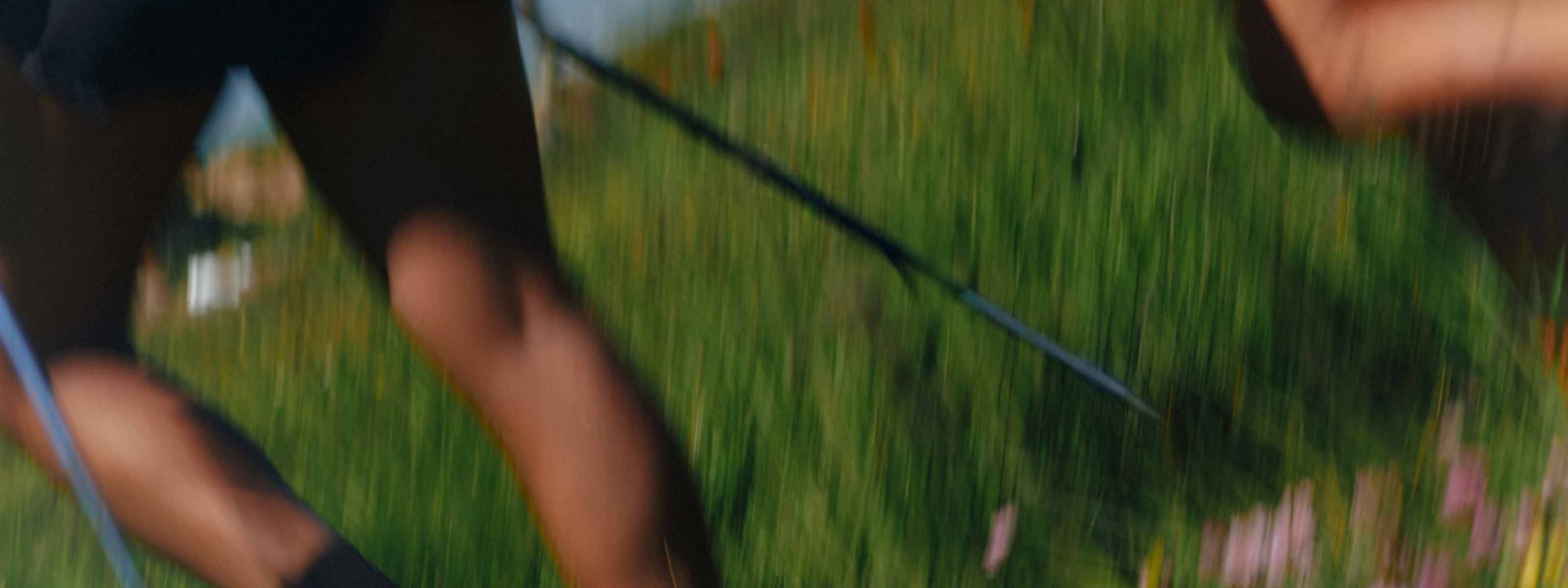 Blurred shot of legs moving through a green field with a leash or strap in hand.