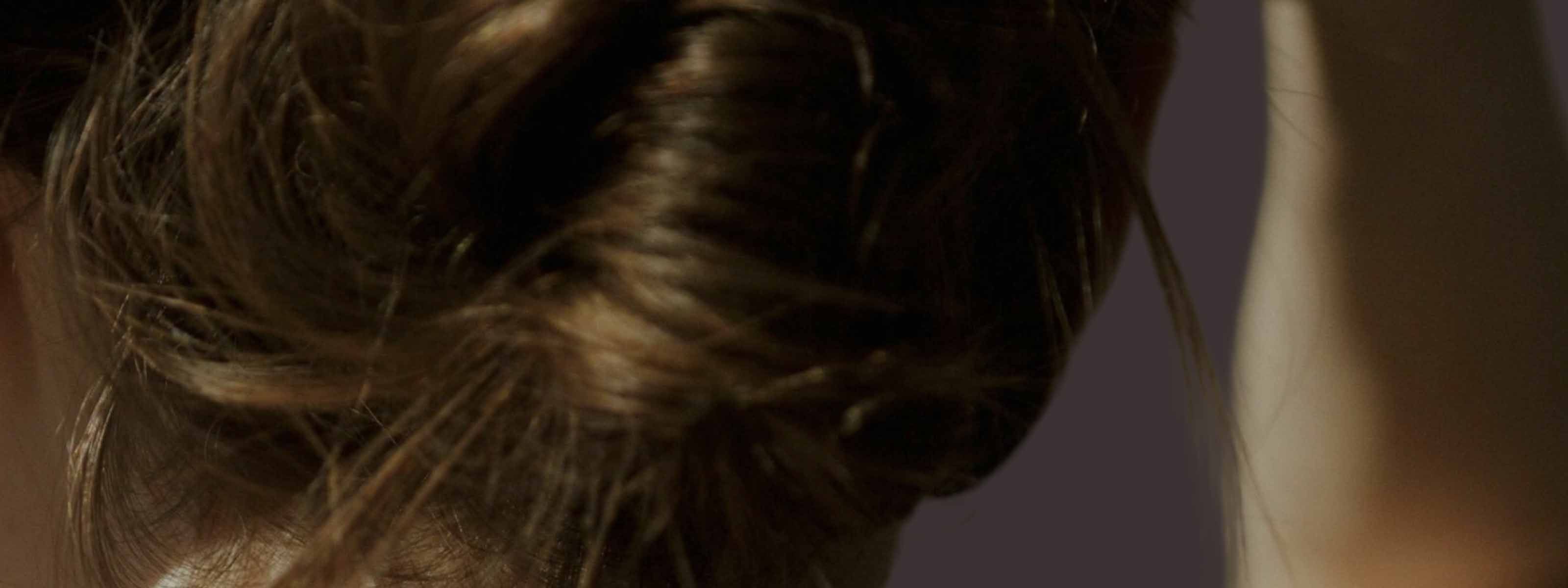Woman's back of head with a loose updo and gold hoop earring in warm, moody lighting.