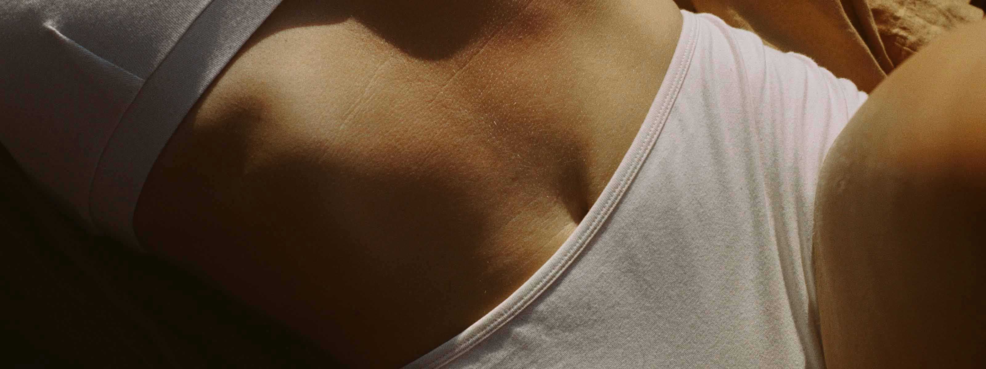Close-up of a stomach and chest in a white tank top and shorts with warm, dramatic sunlight.