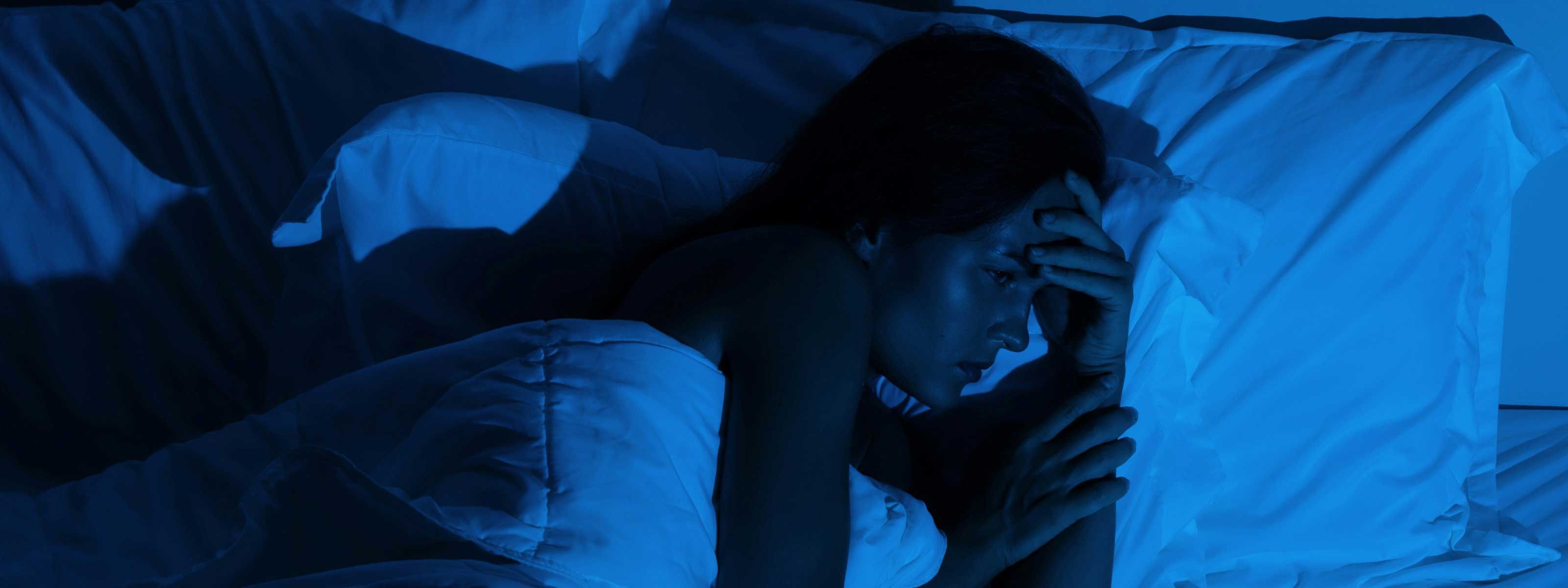 A woman laying a awake in bed with moody lighting
