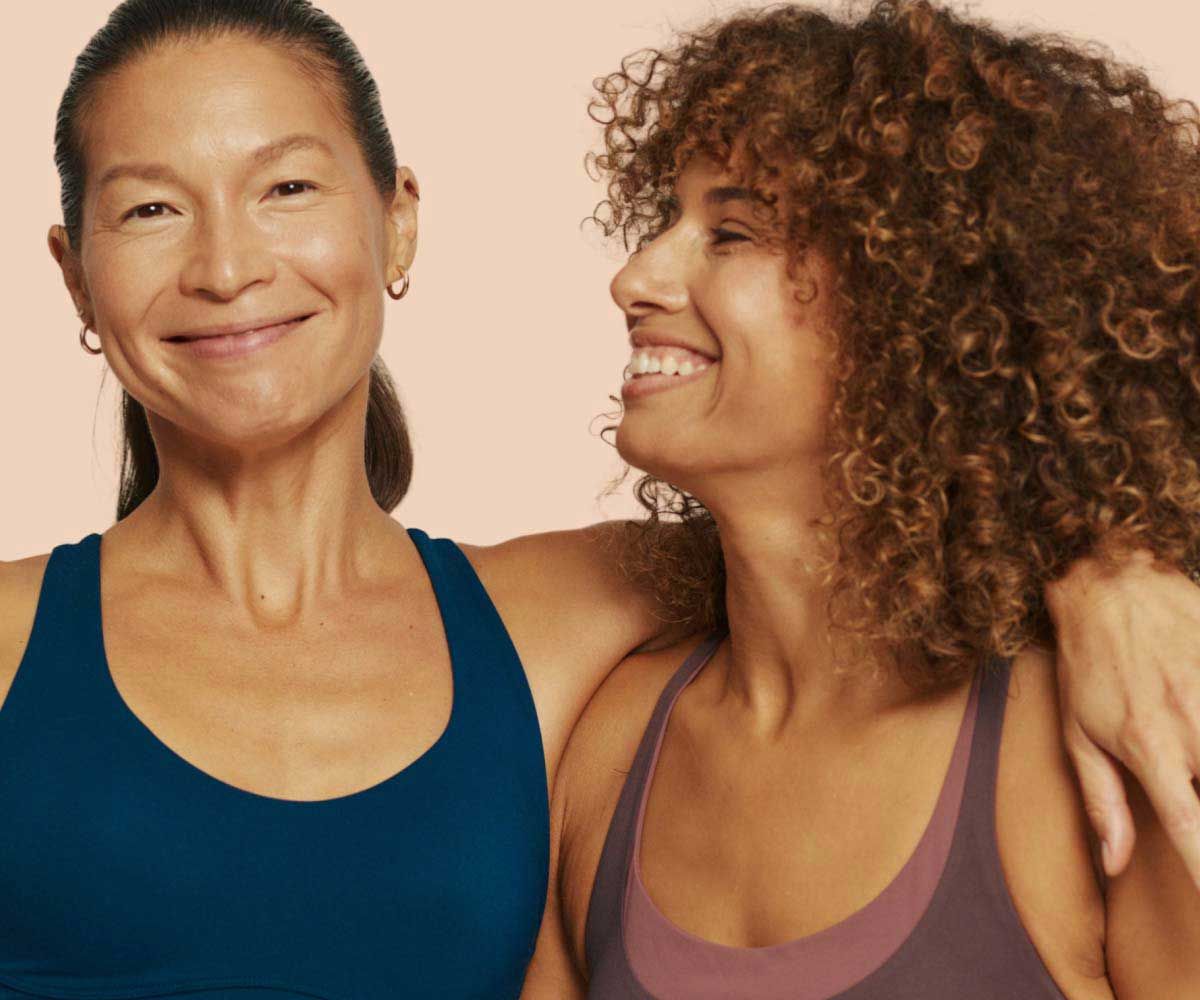 2 smiling women wearing exercise clothing with a cream background