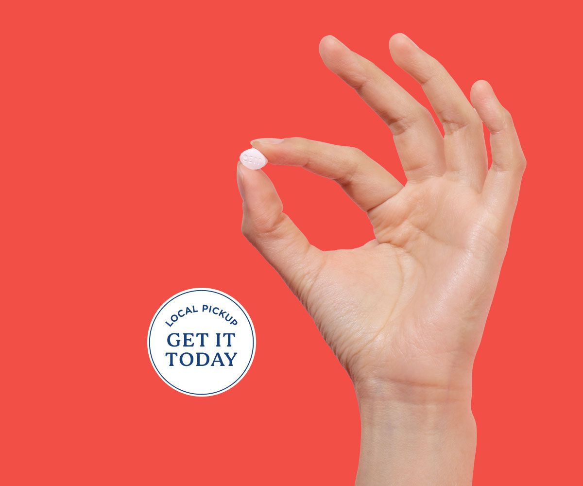Hand holding fluconazole pill for same-day yeast infection treatment on a red background