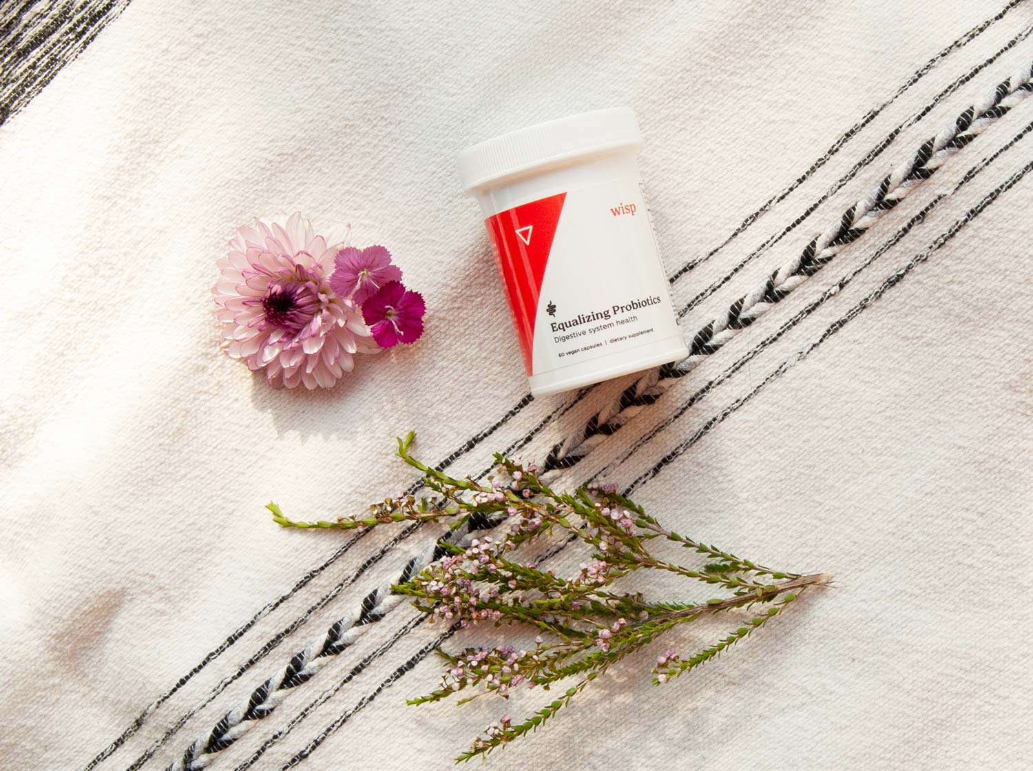 A bottle of Wisp Equalizing Probiotics on a blanket with herbs next to it