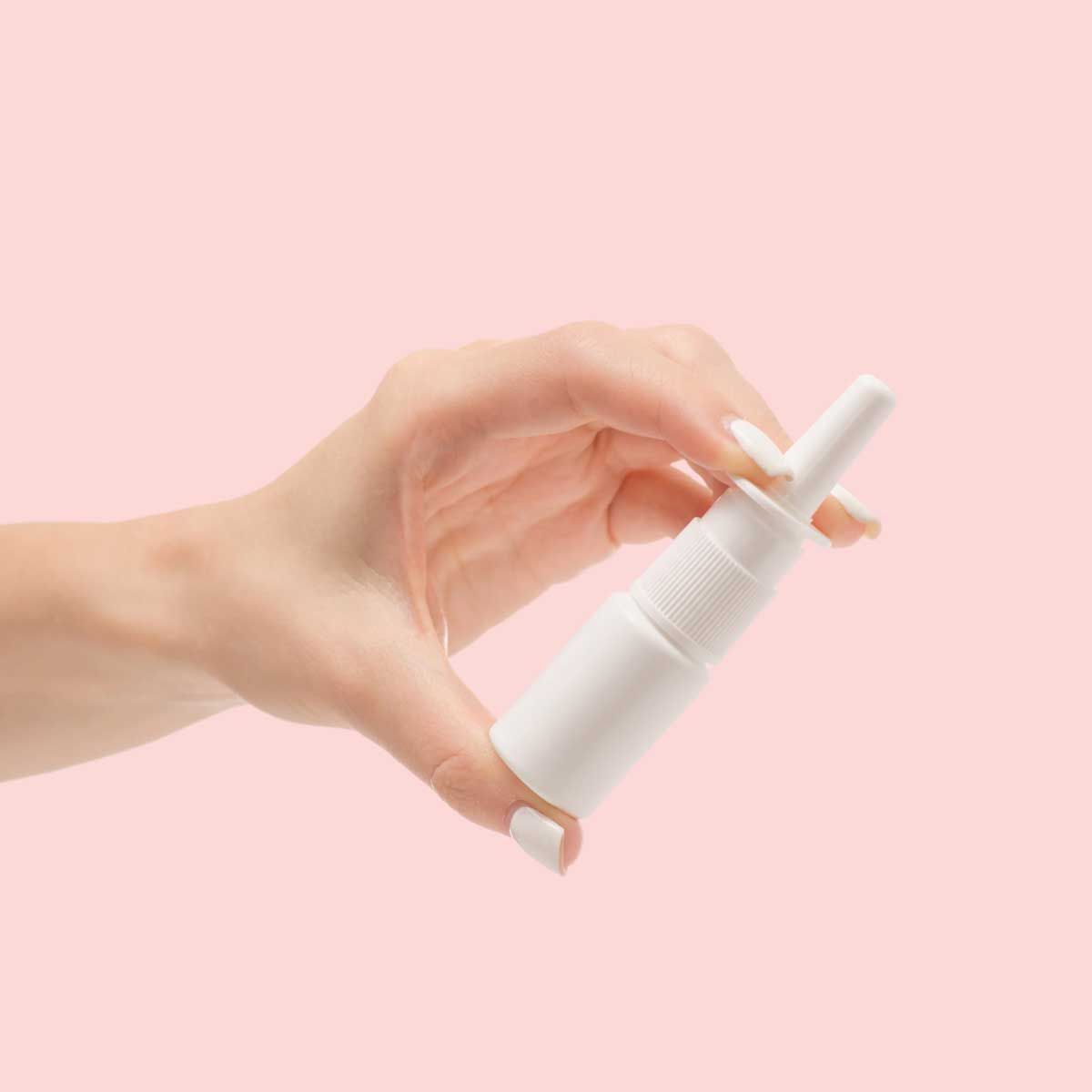A person's hand holding a white nasal spray bottle with a pink background