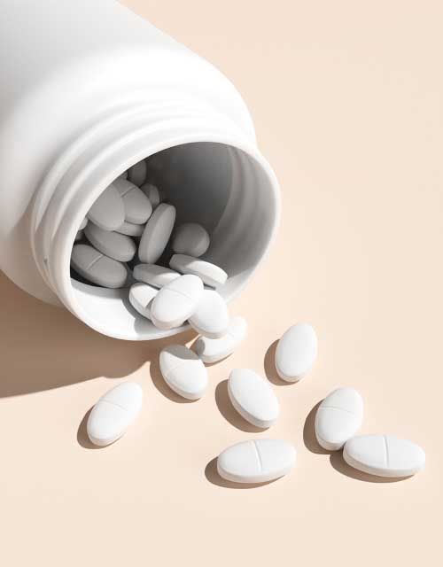 A white bottle with small white pills pouring out of it on a cream surface