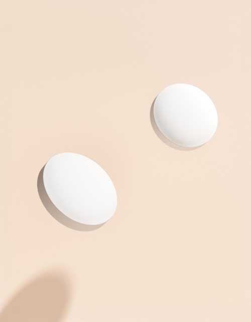 Two emergency contraception pills floating above a cream surface