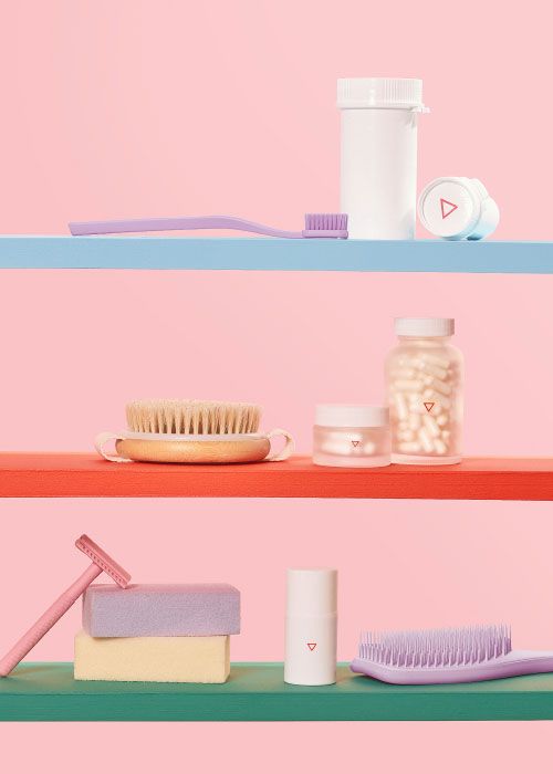 Various Wisp products with a purple toothbrush, purple brush, pink razor and bars of soap on colorful shelves with a pink background