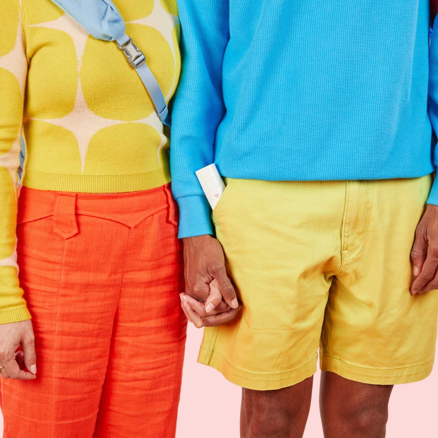 A woman wearing a yellow sweater and orange pants is holding hands with a male wearing a blue sweater and yellow pants