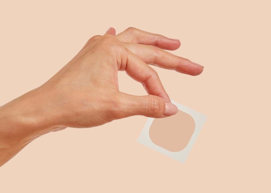 A woman's hand holding a patch on a cream background