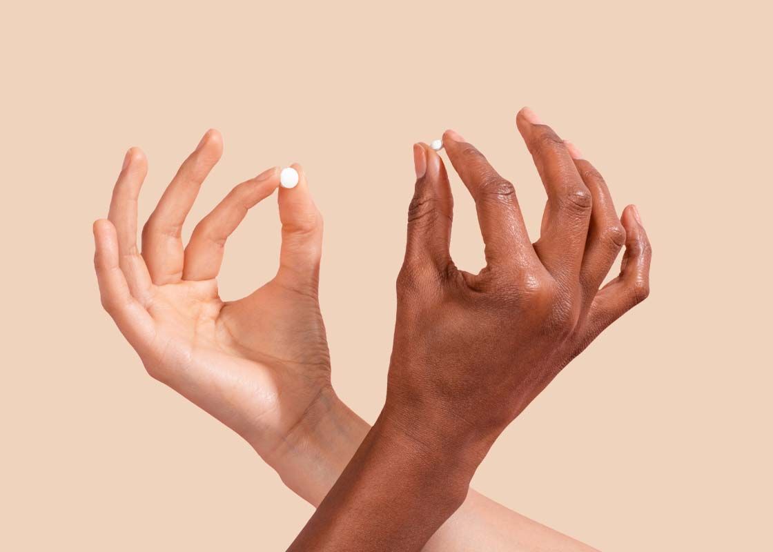 Two woman's hand intertwined with a white pill in each on a cream background