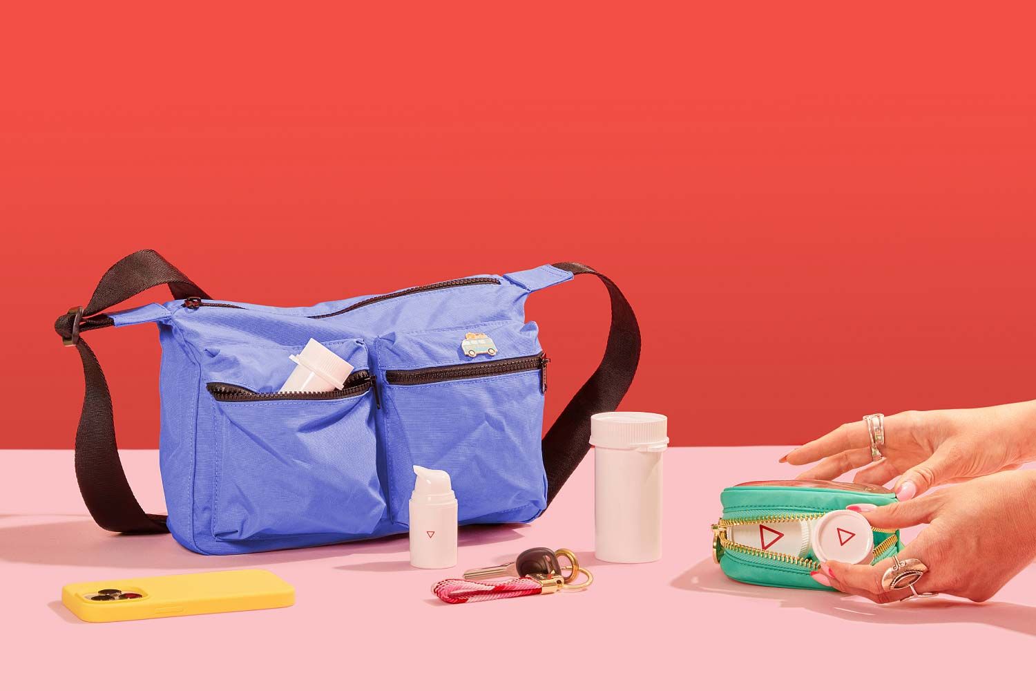 A woman's hands grabbing Wisp medication vials from a travel pouch sitting on a pink surface with a mobile phone, keys and a larger travel bag