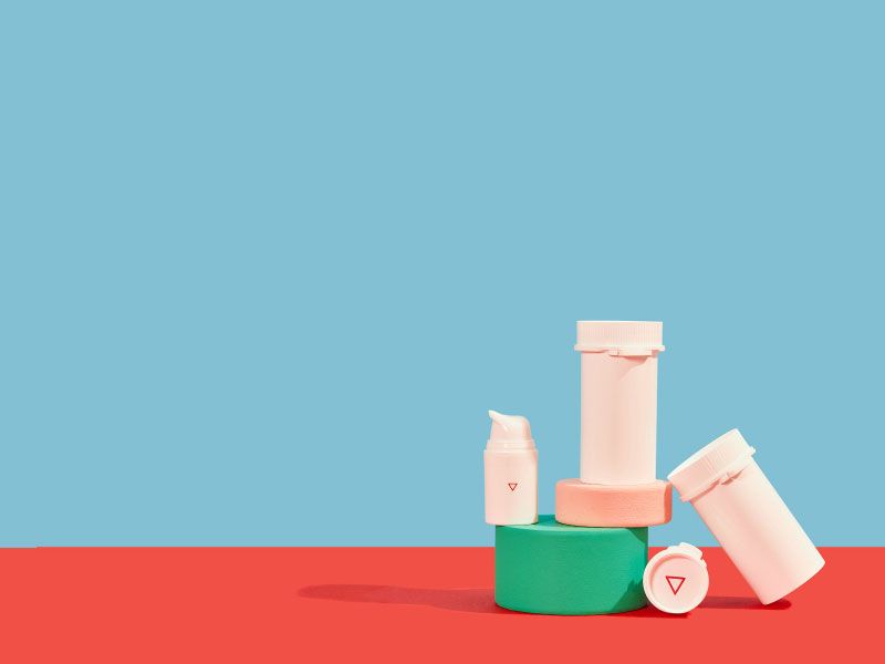 Wisp plastic pill vials and a pump bottle balanced on colorful abstract shapes on a red surface with a light blue background