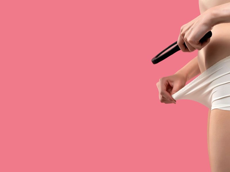 A woman standing with a magnifying glass looking inside her underwear over a rose-colored background