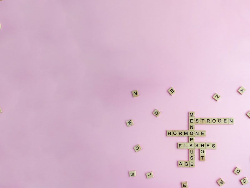Scrabble tiles spelling out. menopause symptoms with various scattered tiles around it on a purple surface