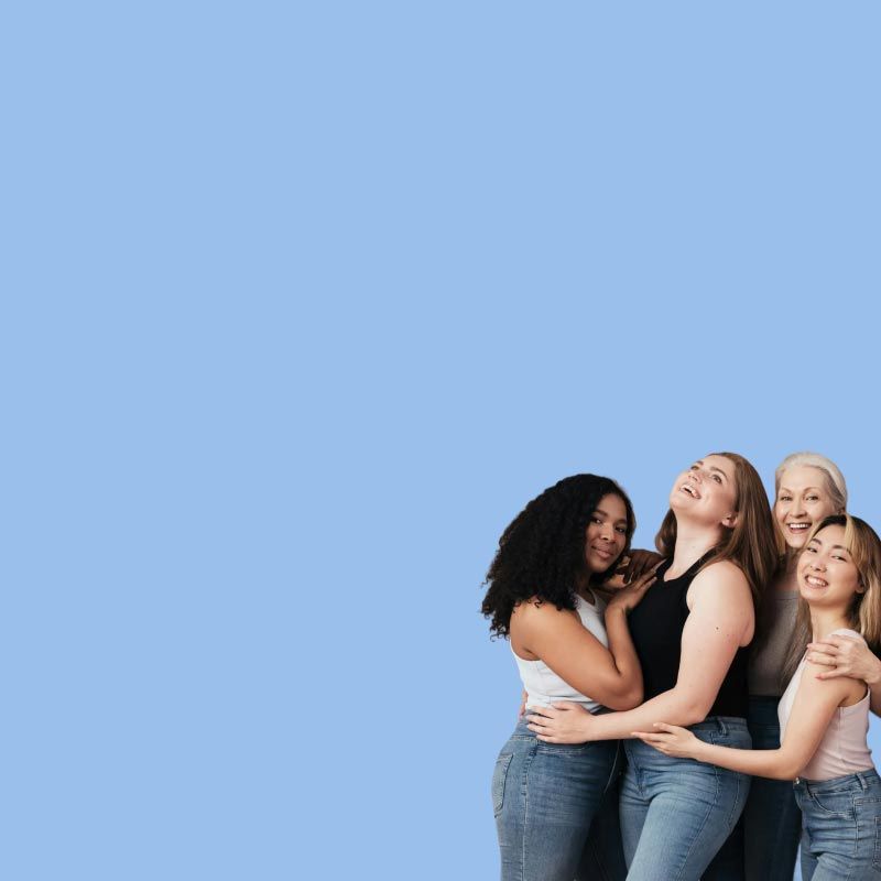 A group of women of different ages and races smiling and hugging each other in front of a light blue background