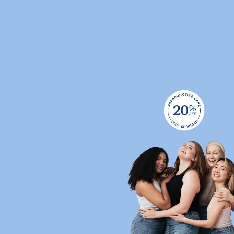 A group of women of different ages and races smiling and hugging each other in front of a light blue background