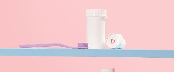 Wisp pill vials and a purple toothbrush on a light blue shelf with a pink background