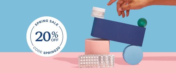 A Wisp glass pill jar and multiple birth control packets balanced on colorful abstract shapes on a pink surface with a light blue background