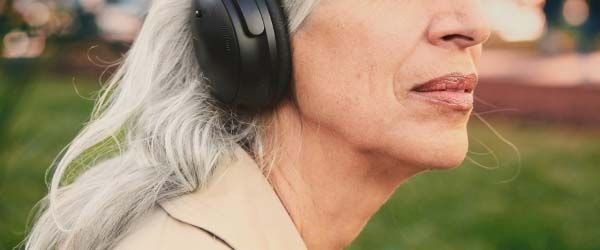 A close up of an older woman wearing headphones and a trench coat outdoors