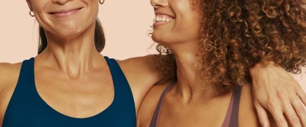 2 smiling women wearing exercise clothing with a cream background