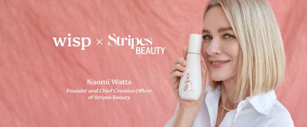 Naomi Watts wearing a white collar shirt while holding a bottle of Oh My Glide by Stripes Beauty on a pink background