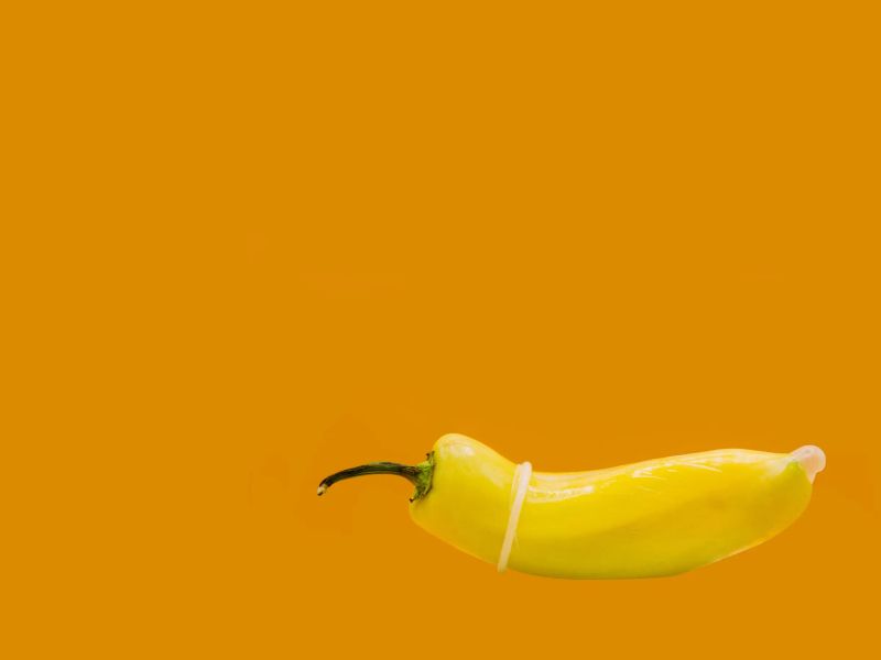 A yellow pepper with a condom on it in front of an orange background