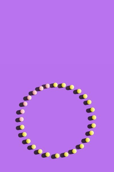 Pink and yellow birth control pills making a circle on a purple surface