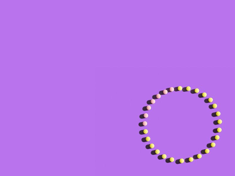 Pink and yellow birth control pills making a circle on a purple surface