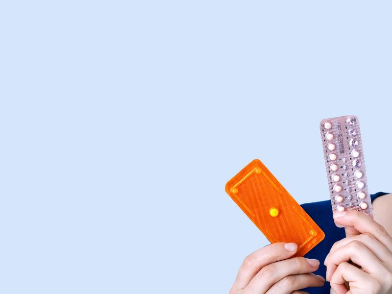 Woman holding an Emergency Packet and a Birth Control packet or a gray blue background