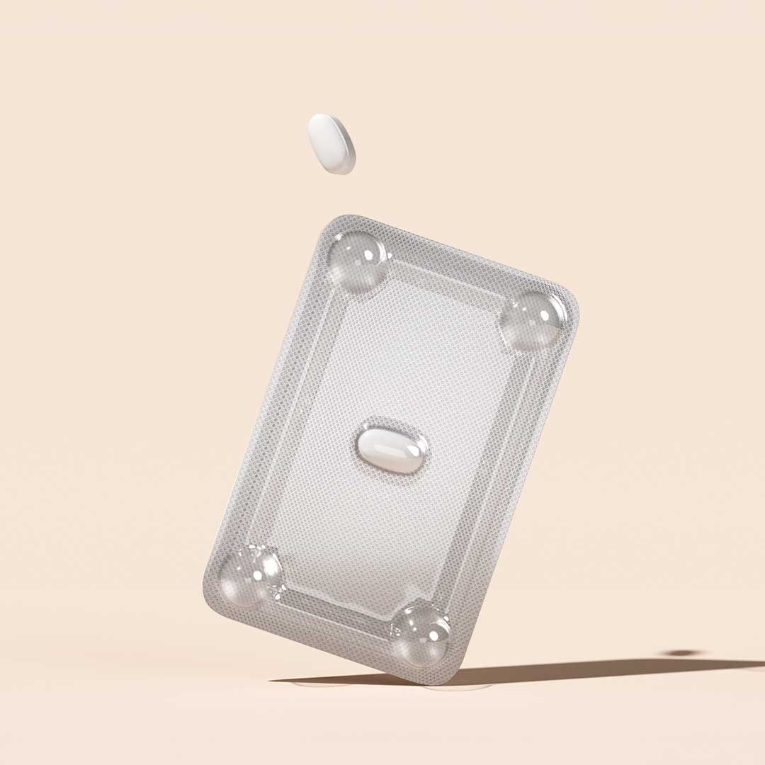A foil pill packet and a white pill floating above it on a cream surface