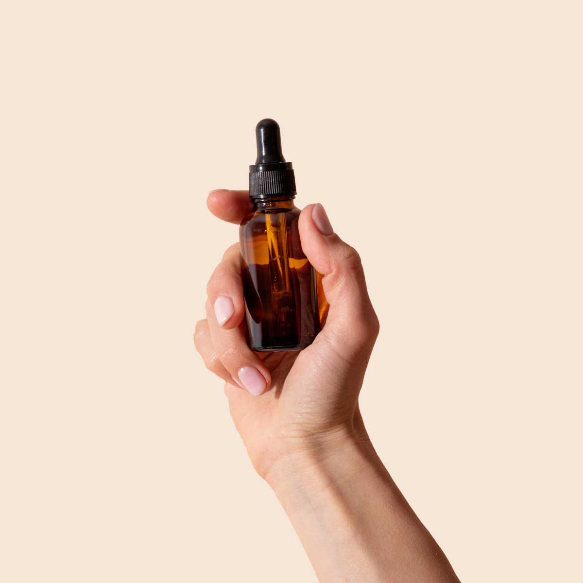 A person's hand holding a dropper bottle with a cream background