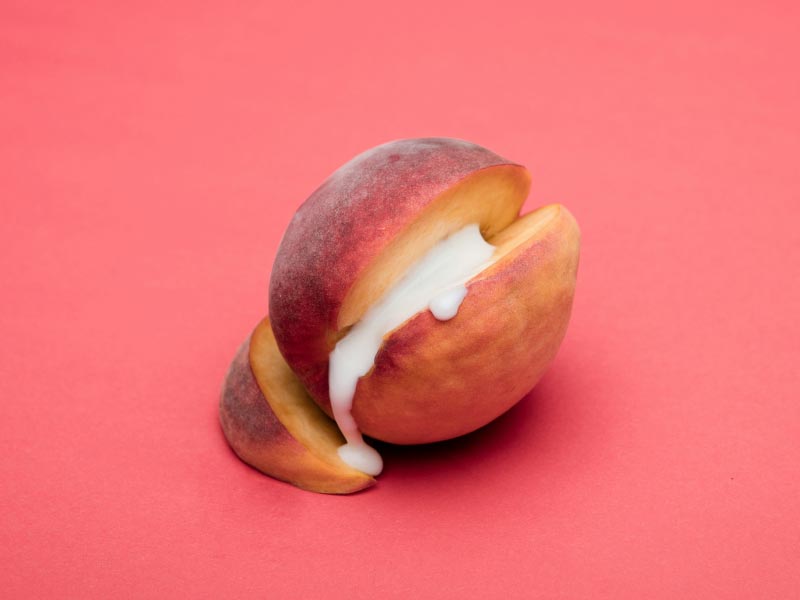 A cut open apricot with a cream substance in the middle on a red background