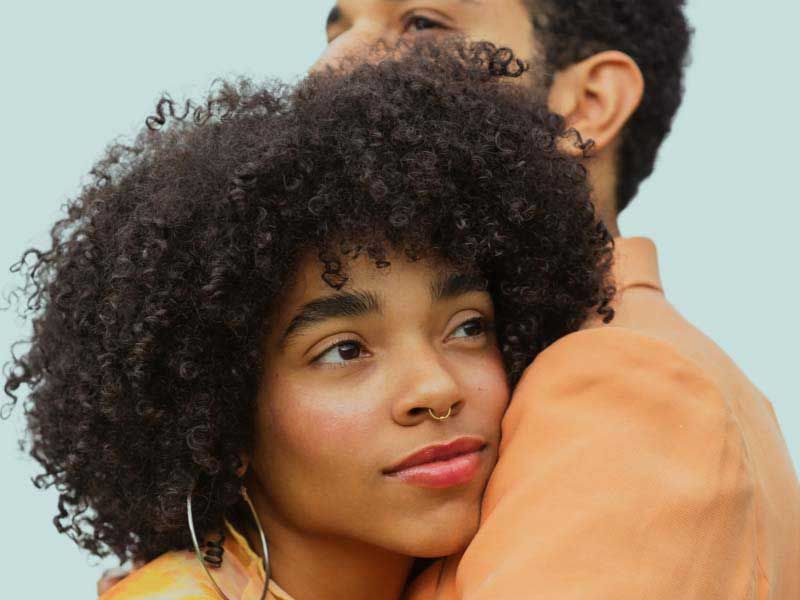 Couple embracing, looking ahead against a plain sky background