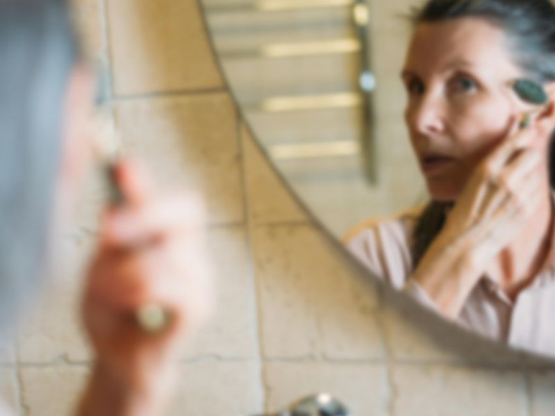 A woman examining her face closely in a bathroom mirror.