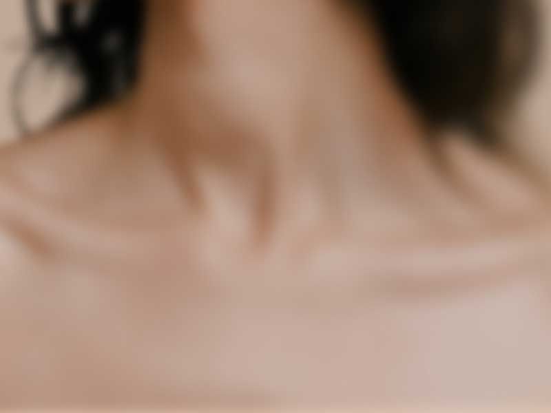 Close up of the neck and shoulders of a woman against a beige background