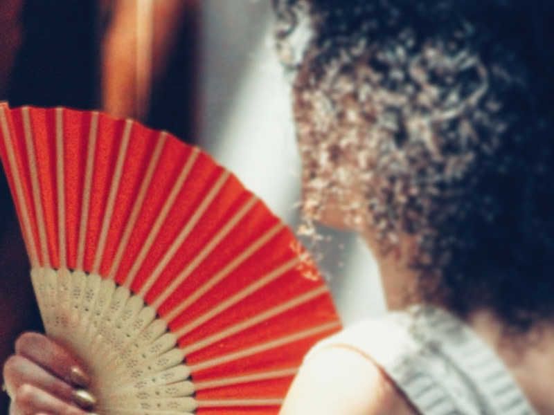 woman with curly hair holding a red hand feathered fan