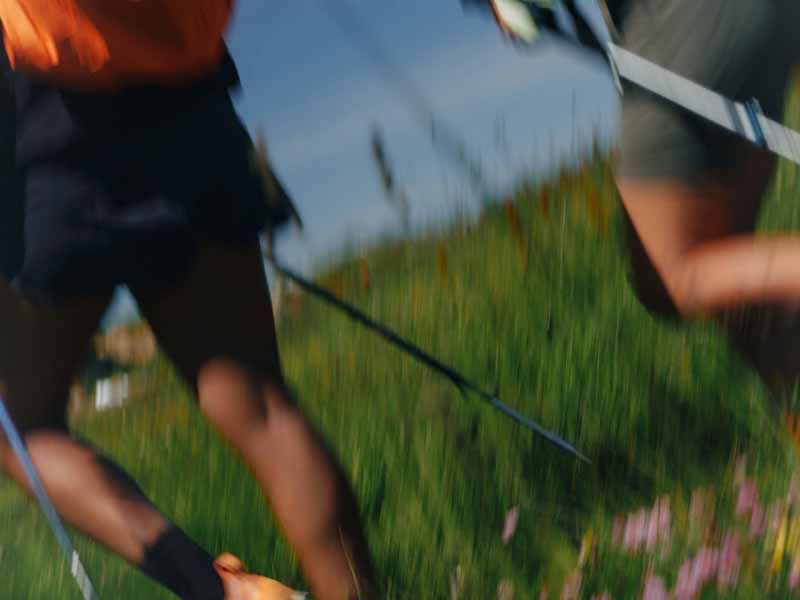 Blurred shot of legs moving through a green field with hiking pole in hand.