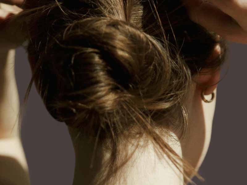 Woman's back of head with a loose updo and gold hoop earring in warm, moody lighting.