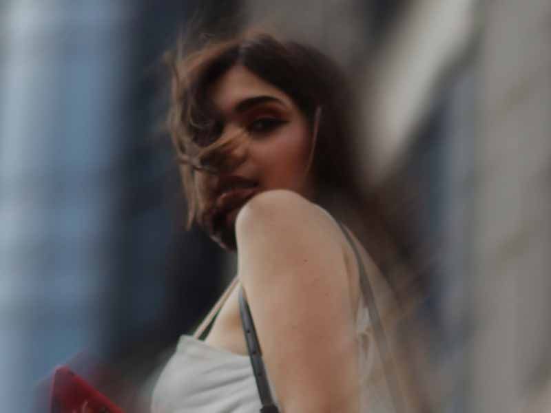 Woman with windswept hair looking over her shoulder in front of a blurred city building.