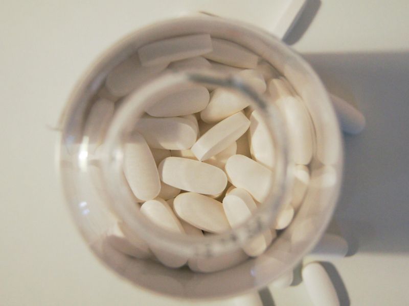 Open bottle filled with white oval tablets viewed from above