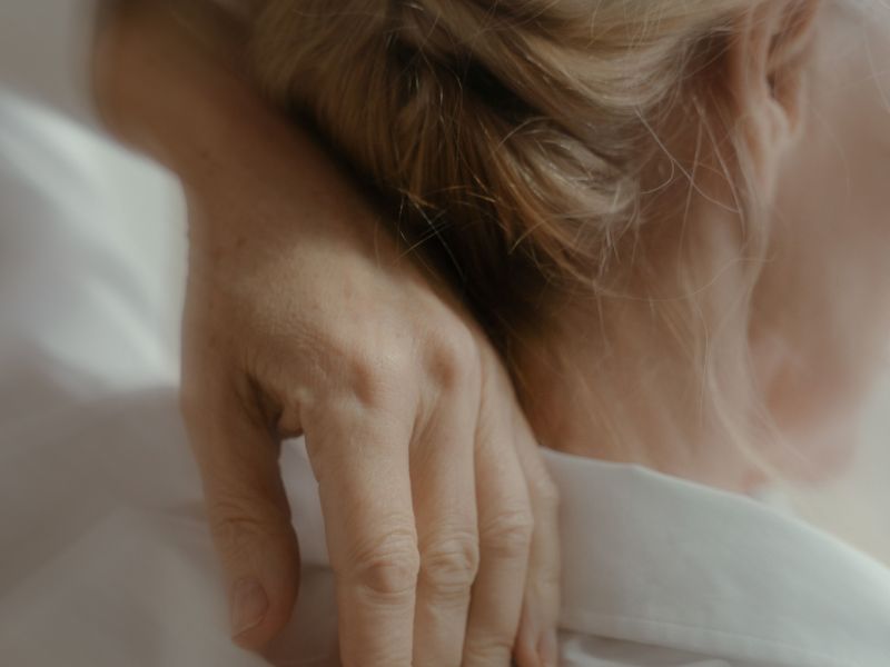 image of the back of a woman's neck with her hand touching her neck and blonde hair