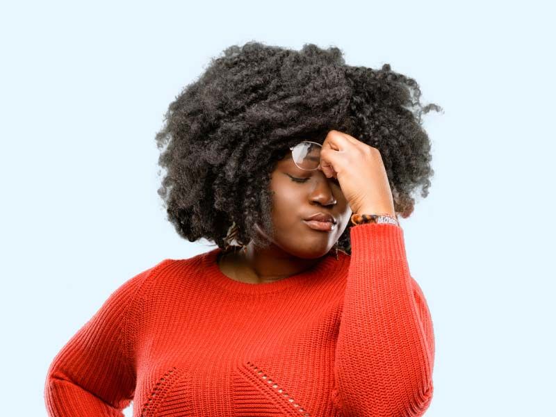 A woman wearing a red sweater is pinching the bridge of her nose in discomfort